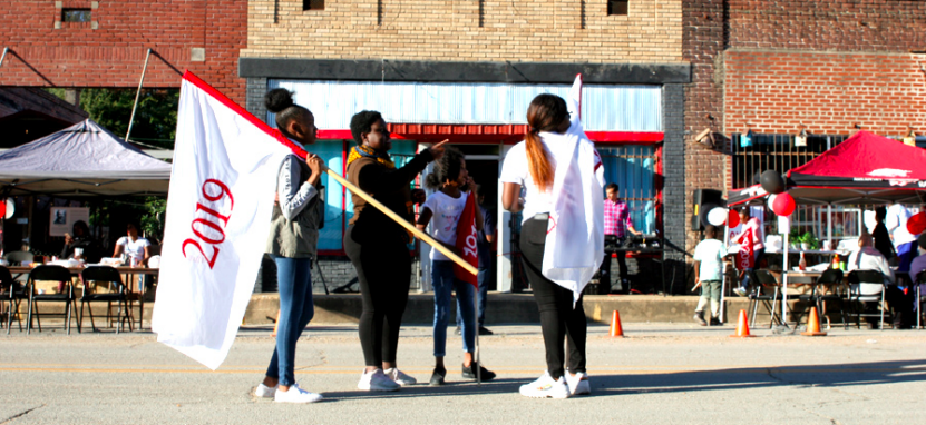 Flag-bearers Kai Mitchell (right), Paris Magsby (middle) and Shakira Zachary (left) gather on Main Street in Elaine with Arielle to learn their movement in the street. They look to the right to take in notes and landscape.